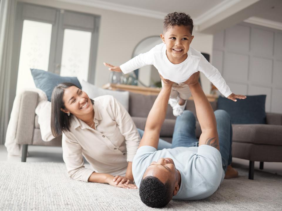 Family playing and smiling on the floor of their living room and father holding up his son.